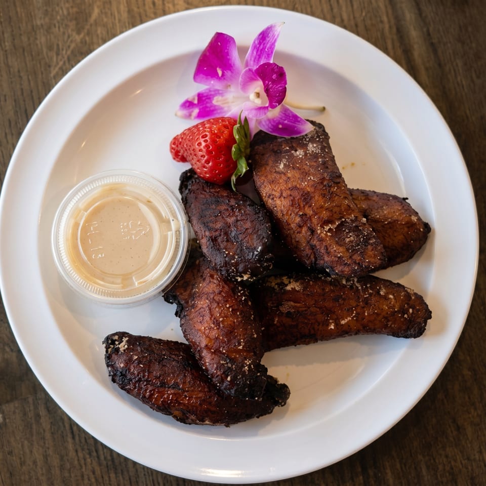 Crispy fried chicken wings with dipping sauce, a strawberry, and an orchid on a white plate.
