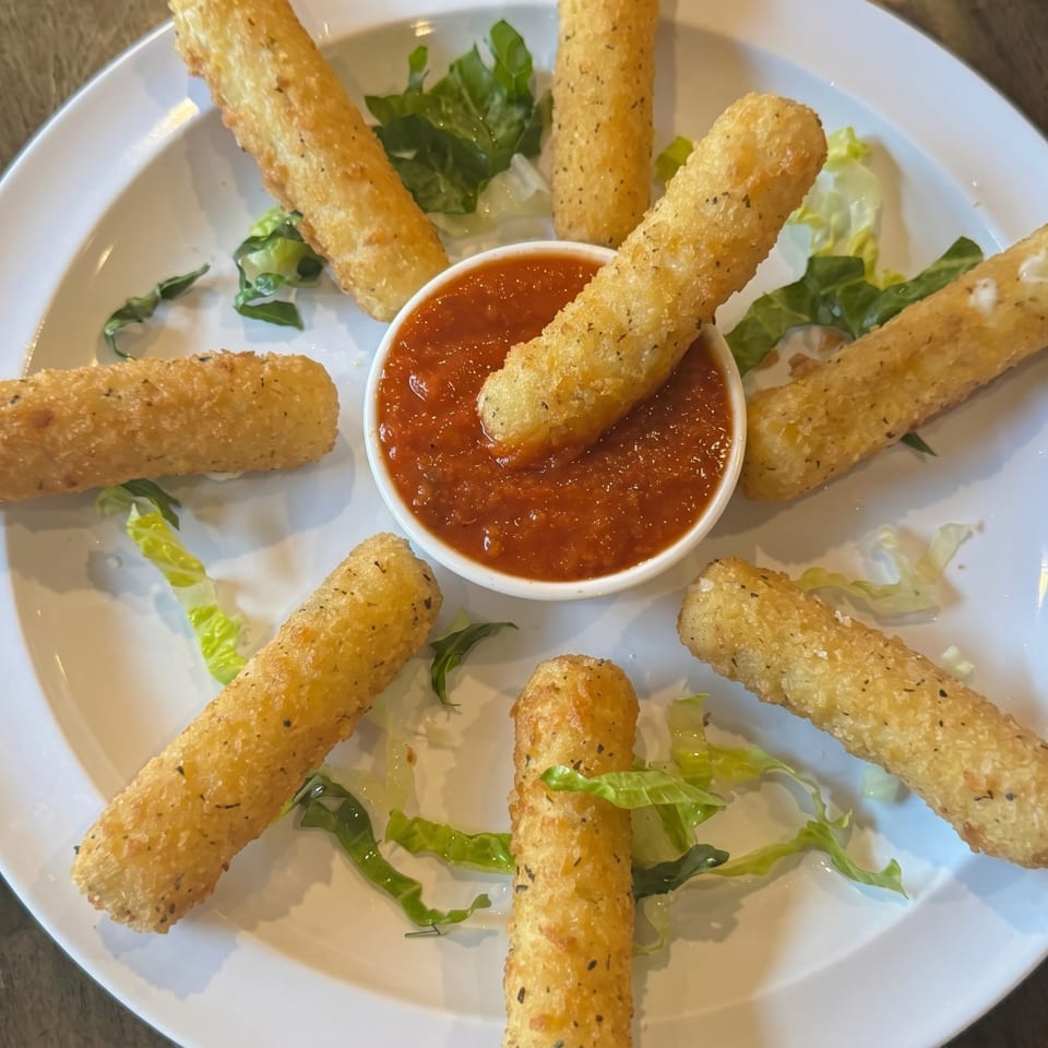 Golden-brown mozzarella sticks arranged around a bowl of red marinara sauce on a white plate.